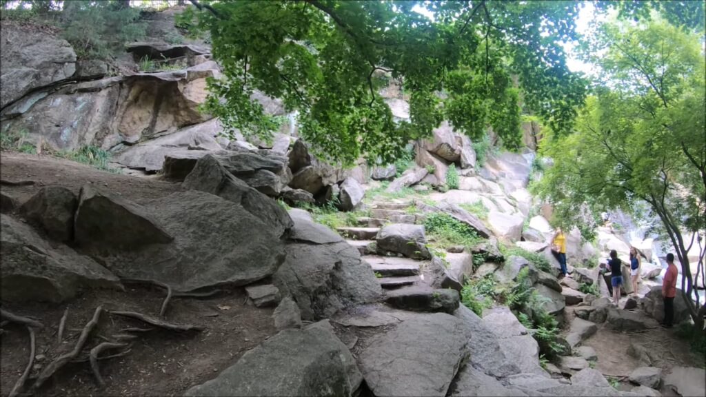 Visitors climb a rocky path beside a cascading waterfall in a green park