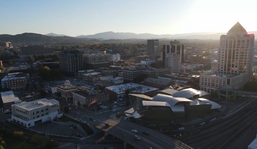  a city with different buildings at sunset, the mountains behind the city